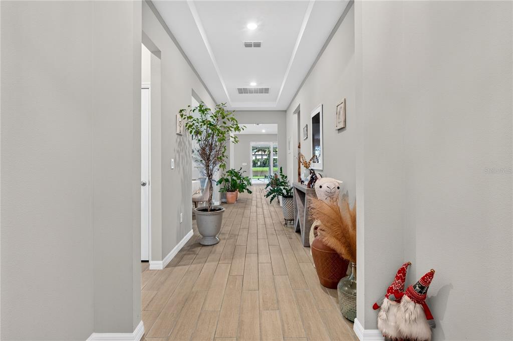 A long hallway with light wood-look tile flooring leads toward a glass door and backyard view — 3329 BIG SKY WAY, LAKEWOOD RANCH, FL