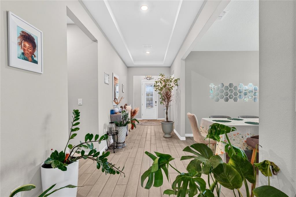A bright entryway with light wood-look tile flooring leads toward a front door and dining area — 3329 BIG SKY WAY, LAKEWOOD RANCH, FL