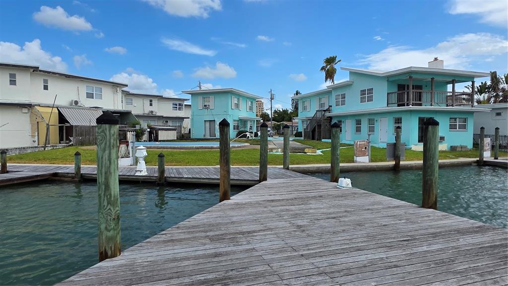 A wooden dock extends toward a turquoise building and a swimming pool by the water — 627 BAY ESPLANADE, CLEARWATER BEACH, FL