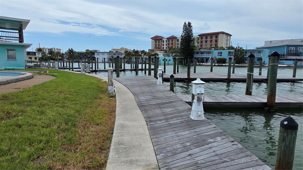 A wooden dock extends from a grassy lawn toward a canal with nearby buildings — 627 BAY ESPLANADE, CLEARWATER BEACH, FL