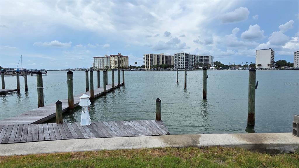 A wooden dock extends into a calm bay with residential buildings visible in the distance — 627 BAY ESPLANADE, CLEARWATER BEACH, FL