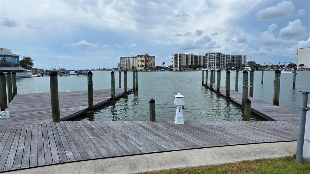 A wooden boat dock extends into a waterway with large apartment buildings in the background — 627 BAY ESPLANADE, CLEARWATER BEACH, FL