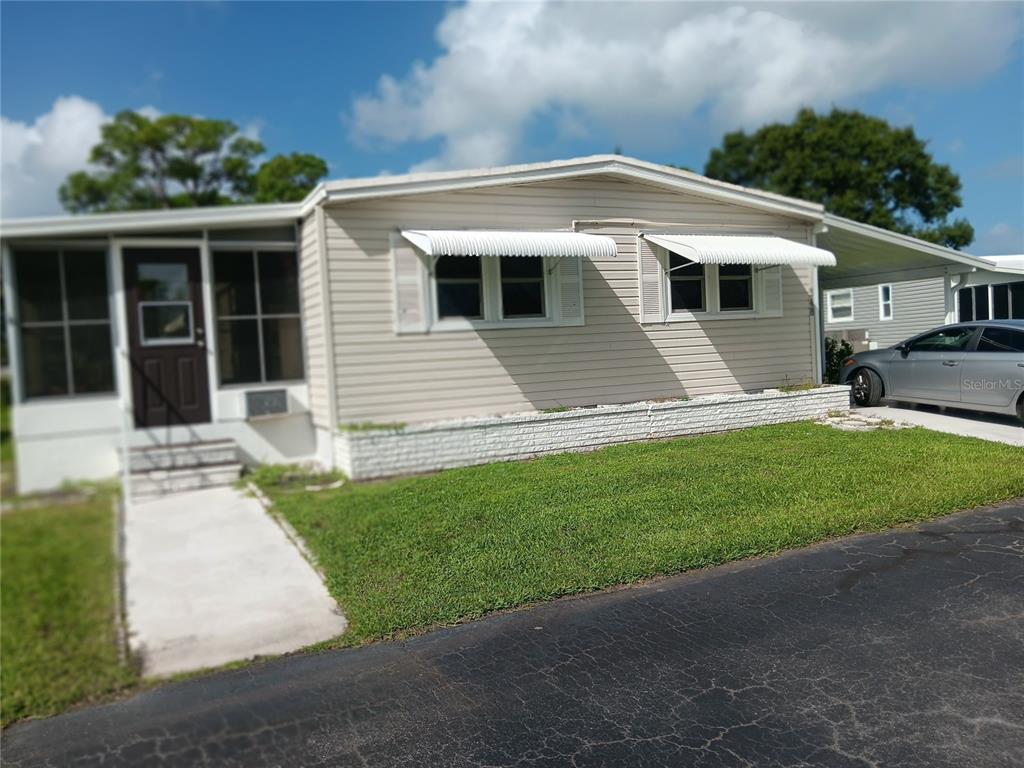 A single-story mobile home with beige siding, white awnings, and a concrete walkway — 348 TROPIC DRIVE, OSPREY, FL