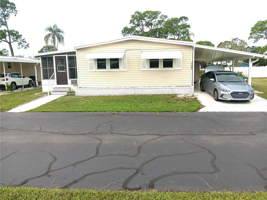 A single-story manufactured home with light siding, white awnings, and an attached carport — 348 TROPIC DRIVE, OSPREY, FL