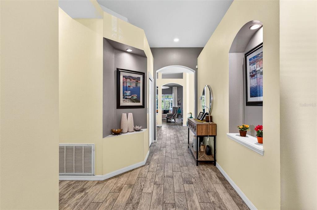 A hallway features wood-look tile flooring, arched wall niches with artwork, and recessed lighting — 11013 ROCKLEDGE VIEW DRIVE, RIVERVIEW, FL