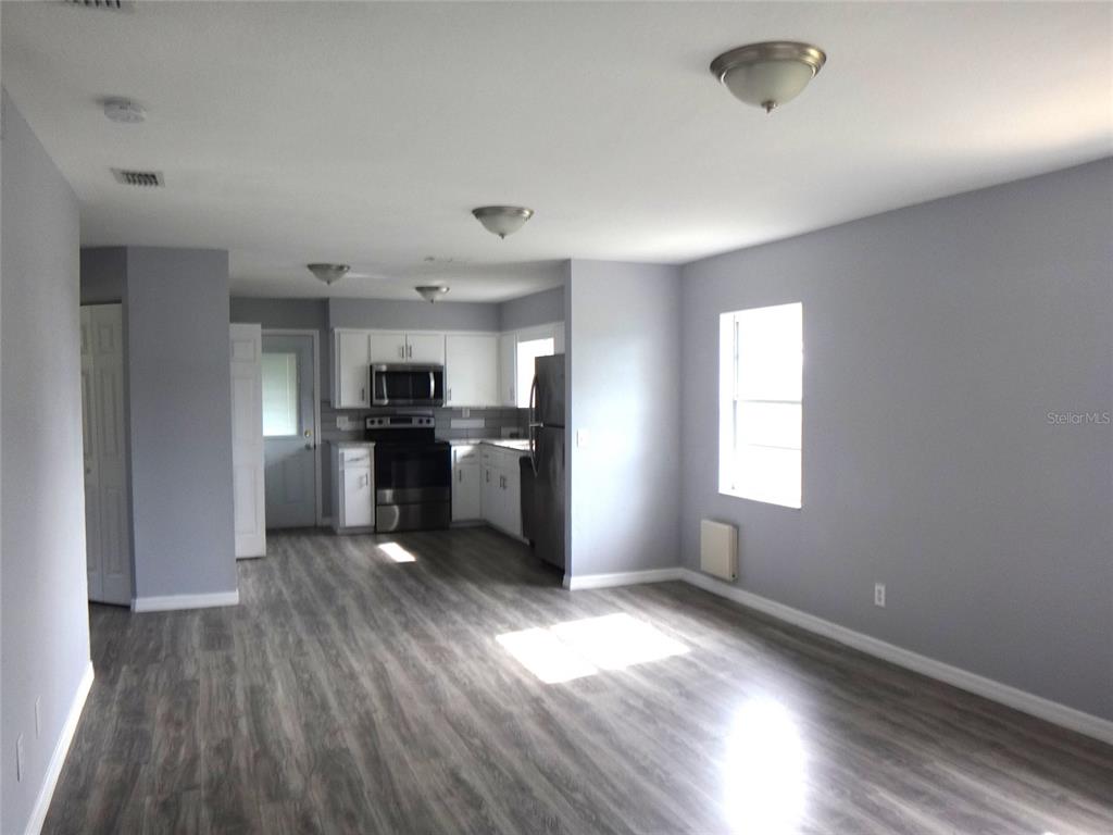 An open-concept kitchen and living area features gray walls, wood-look flooring, and stainless steel appliances — 1125 BRITTS LANE, BARTOW, FL