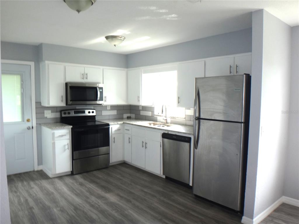 A kitchen with white cabinets, stainless steel appliances, gray tile backsplash, and wood-look flooring — 1125 BRITTS LANE, BARTOW, FL