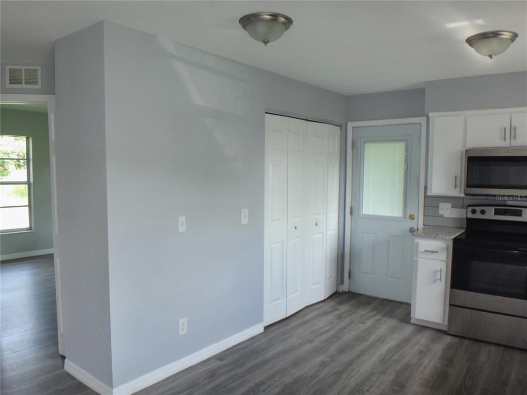 An empty room features gray walls, wood-look flooring, two windows, and a white entry door — 1125 BRITTS LANE, BARTOW, FL