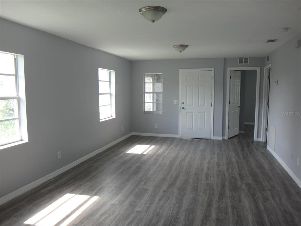 An empty room features gray walls, wood-look flooring, two windows, and a white entry door — 1125 BRITTS LANE, BARTOW, FL