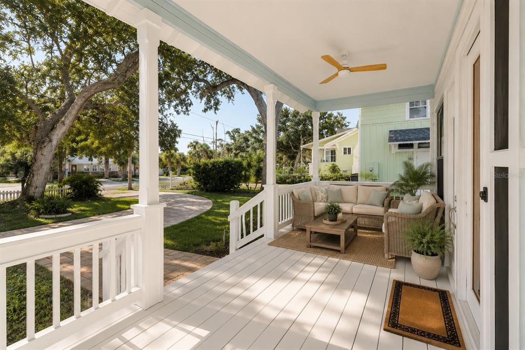 A covered front porch features white railings, wicker seating, a ceiling fan, and wood flooring — 410 S PENINSULA AVENUE, NEW SMYRNA BEACH, FL