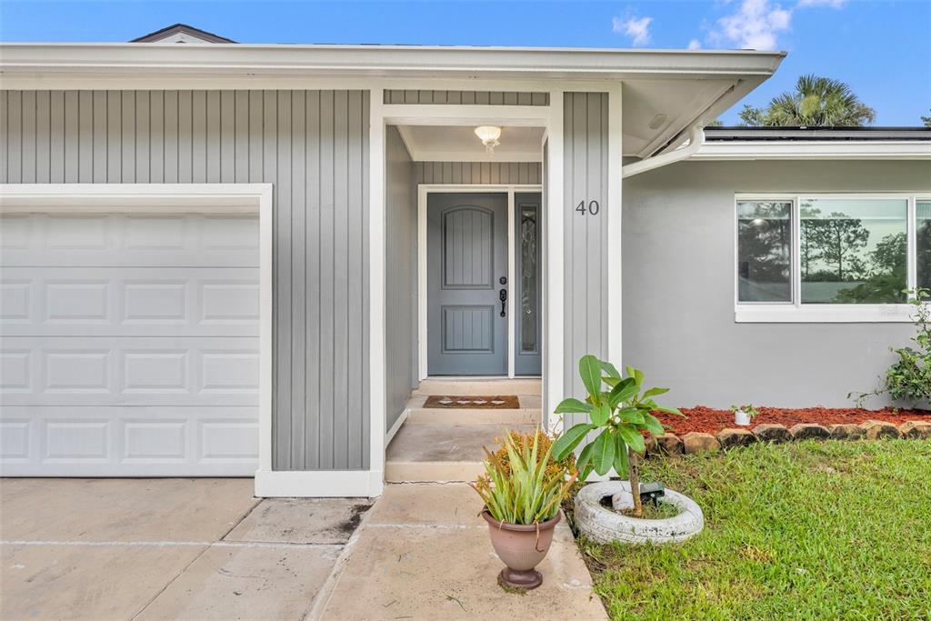 The exterior of a house features a gray front door, vertical siding, and a garage — 40 BLARE DRIVE, PALM COAST, FL