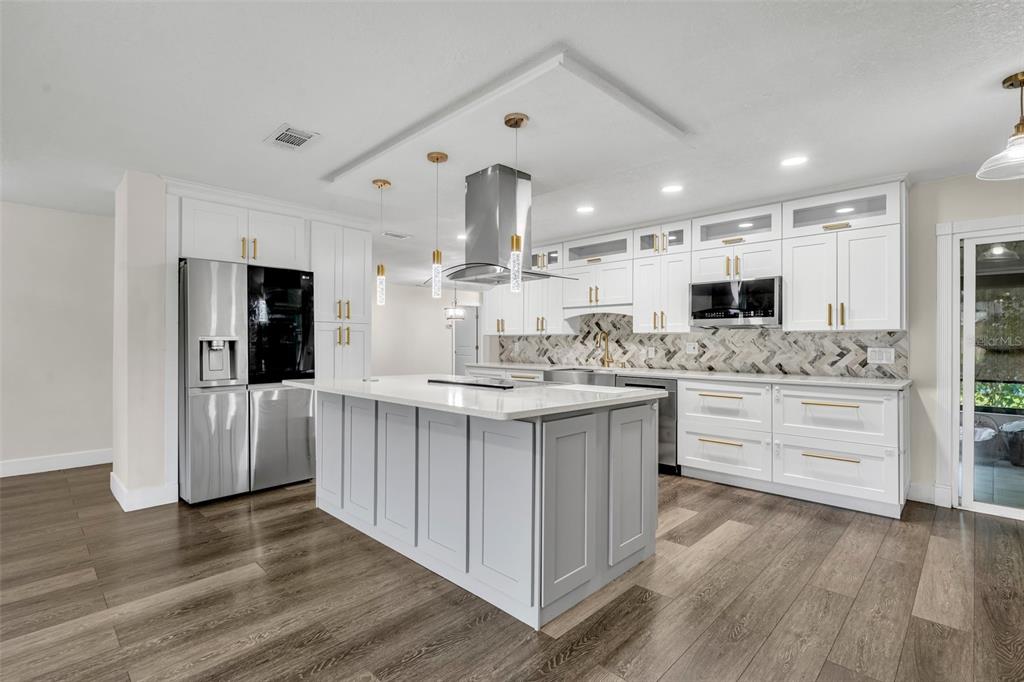 A modern kitchen features white cabinets, a gray island, stainless steel appliances, and wood flooring — 40 BLARE DRIVE, PALM COAST, FL