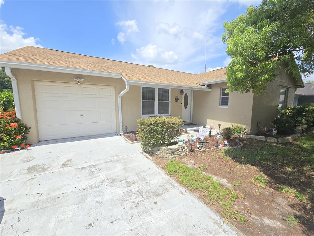 A single-story house with a tan stucco exterior, a one-car garage, and a concrete driveway — 7051 VALLEJO WAY, NEW PORT RICHEY, FL