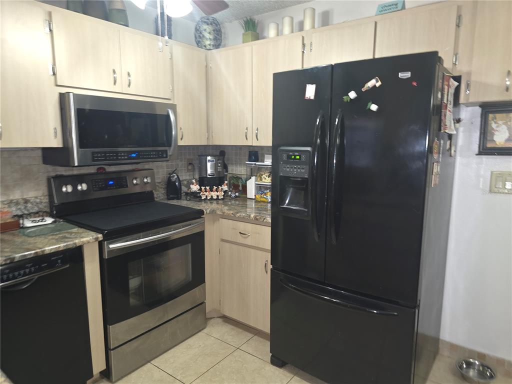 A kitchen features light wood cabinets, stainless steel appliances, a black refrigerator, and tile flooring — 7051 VALLEJO WAY, NEW PORT RICHEY, FL