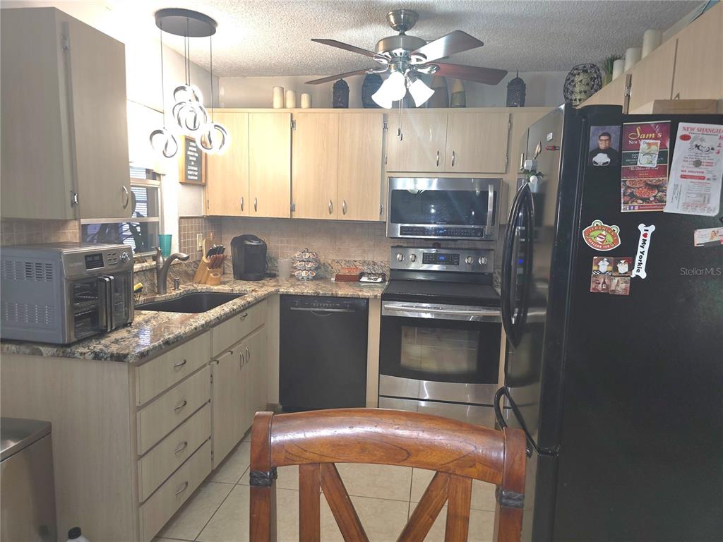 A kitchen features light wood cabinets, granite countertops, stainless steel appliances, and a black refrigerator — 7051 VALLEJO WAY, NEW PORT RICHEY, FL