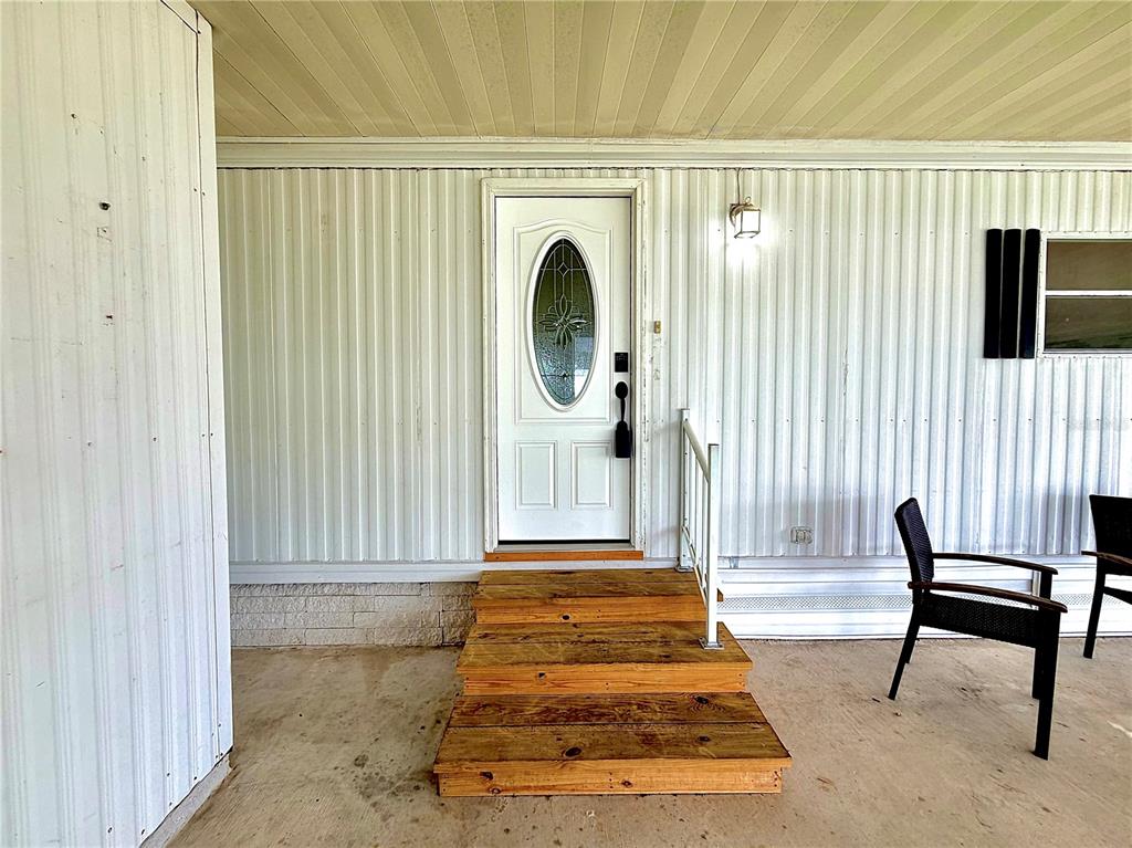 A white front door with an oval glass insert is accessed by wooden steps — 7445 MORIAH AVENUE, BROOKSVILLE, FL