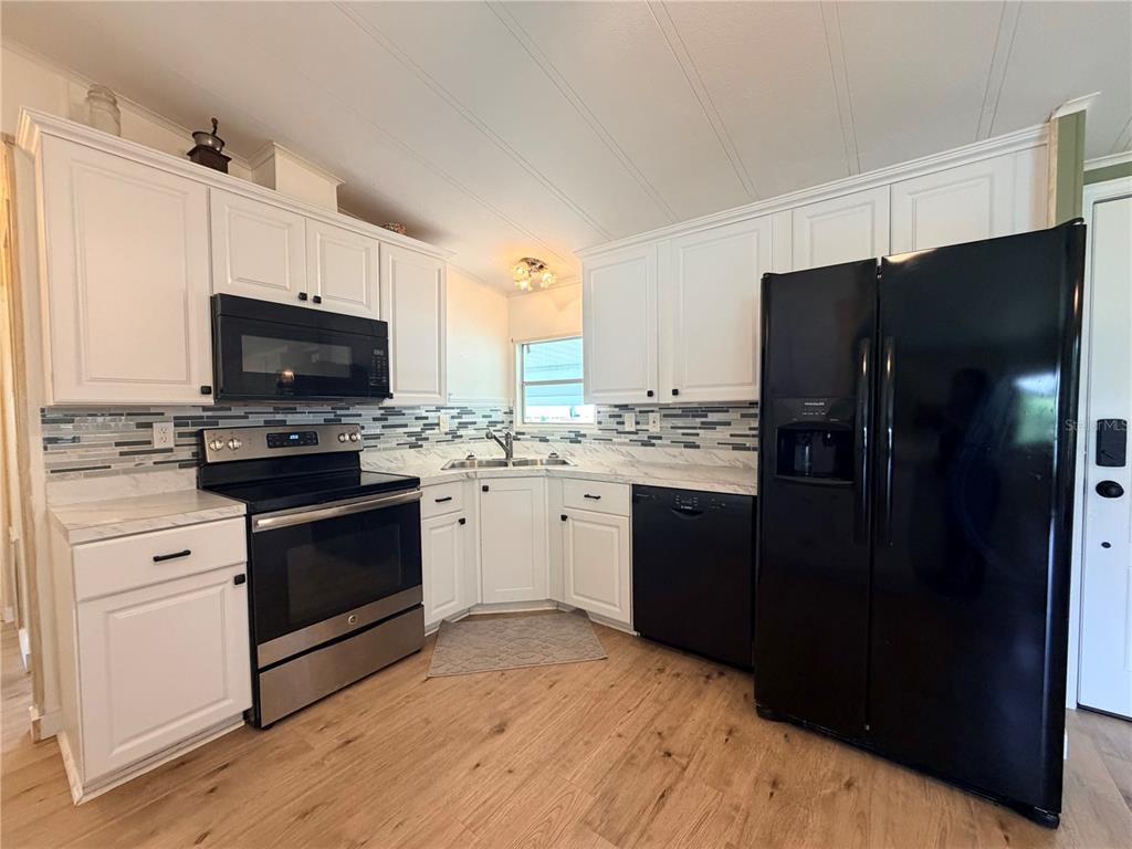 A kitchen with white cabinets, stainless steel appliances, a black refrigerator, and a tiled backsplash — 7445 MORIAH AVENUE, BROOKSVILLE, FL