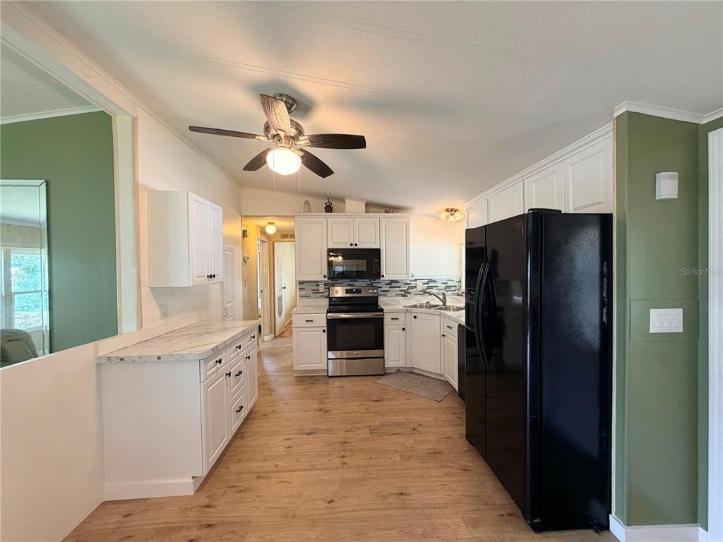A kitchen features white cabinets, stainless steel appliances, a black refrigerator, and wood-look flooring — 7445 MORIAH AVENUE, BROOKSVILLE, FL