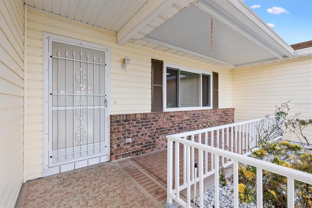 A covered front porch features light yellow siding, a brick accent wall, and a security door — 10767 SE 174TH LOOP, SUMMERFIELD, FL