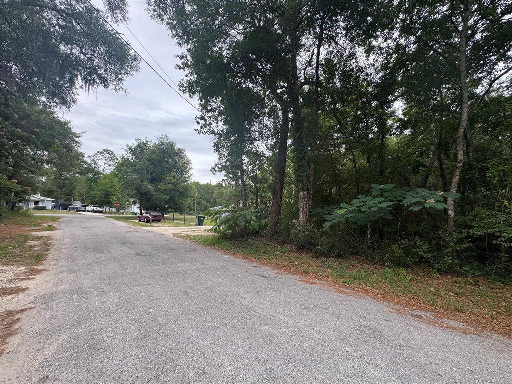 A paved road leads toward a wooded lot with a red car parked nearby — 3462 E MICHAEL STREET, INVERNESS, FL