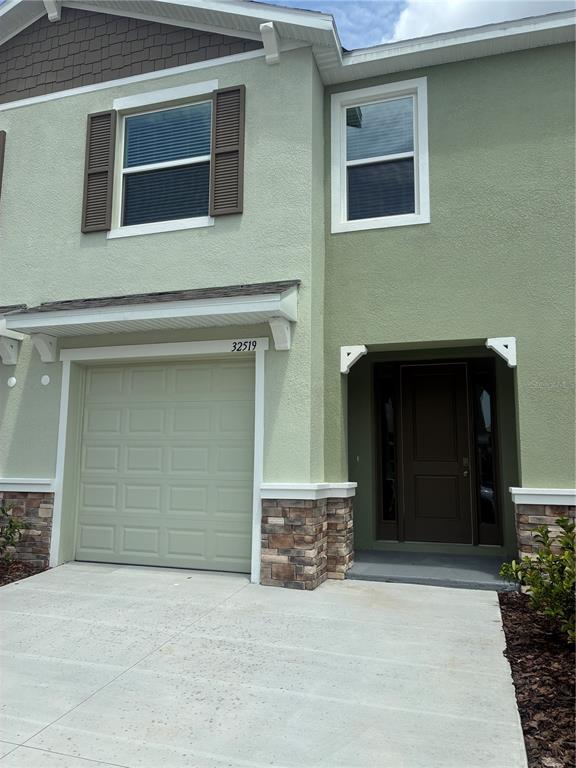 A two-story townhouse exterior features a light green stucco facade, stone accents, and a garage — 32519 MIDSUMMER NIGHT LANE, WESLEY CHAPEL, FL