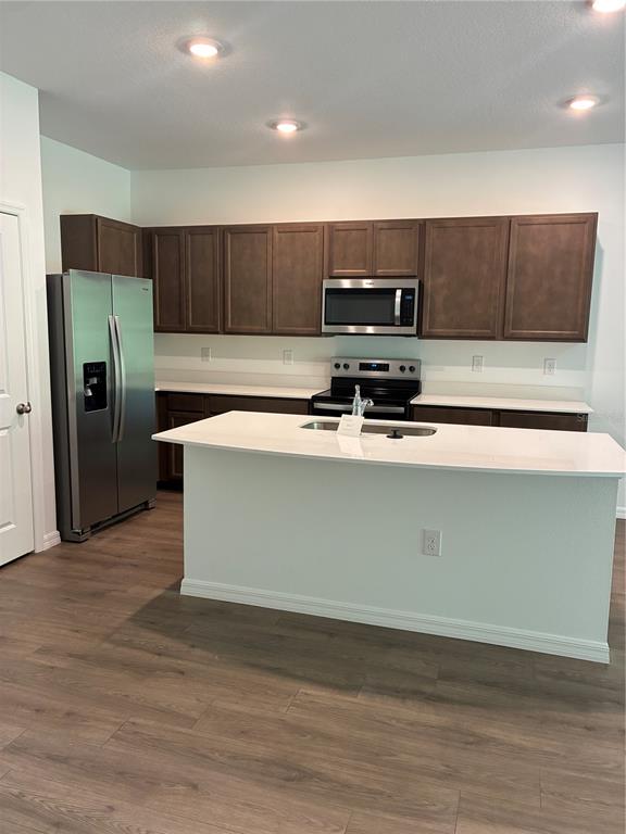 A kitchen features dark wood cabinets, stainless steel appliances, and a white quartz island countertop — 32519 MIDSUMMER NIGHT LANE, WESLEY CHAPEL, FL
