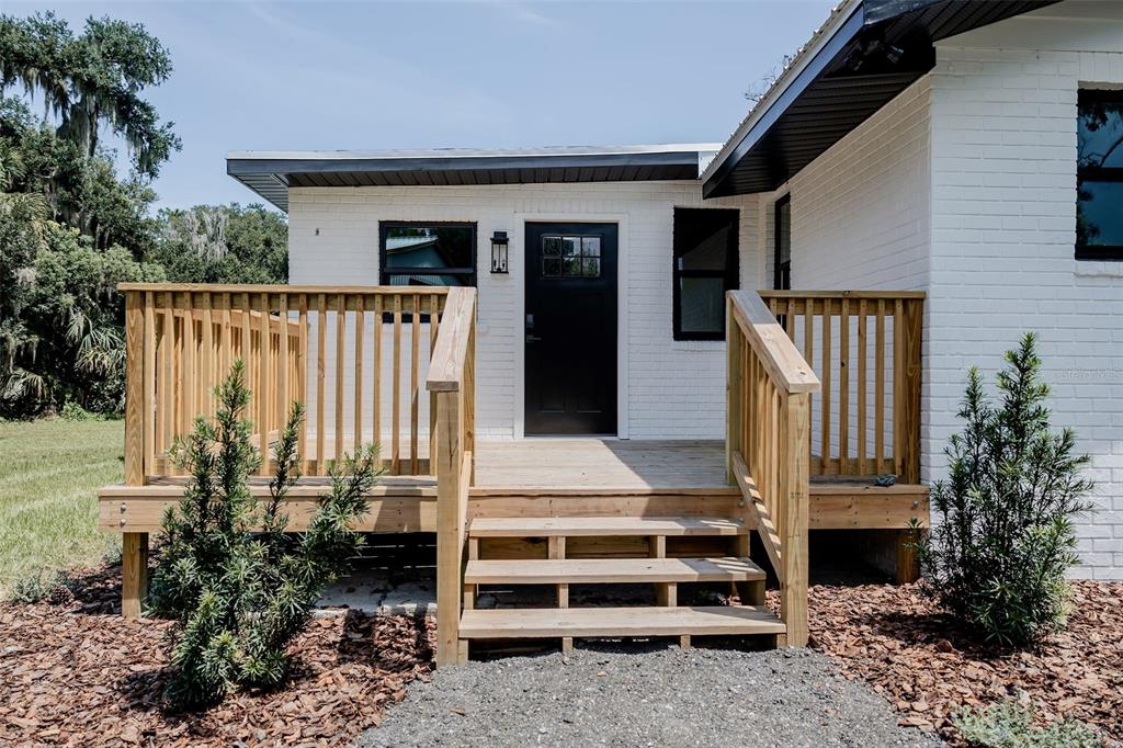 A white brick house exterior features a wooden deck with stairs and a black door — 2463 PIONEER TRAIL, NEW SMYRNA BEACH, FL