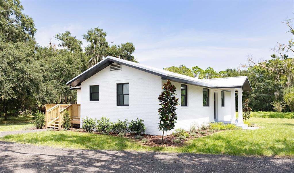 A white brick house with a dark metal roof sits on a grassy, wooded lot — 2463 PIONEER TRAIL, NEW SMYRNA BEACH, FL