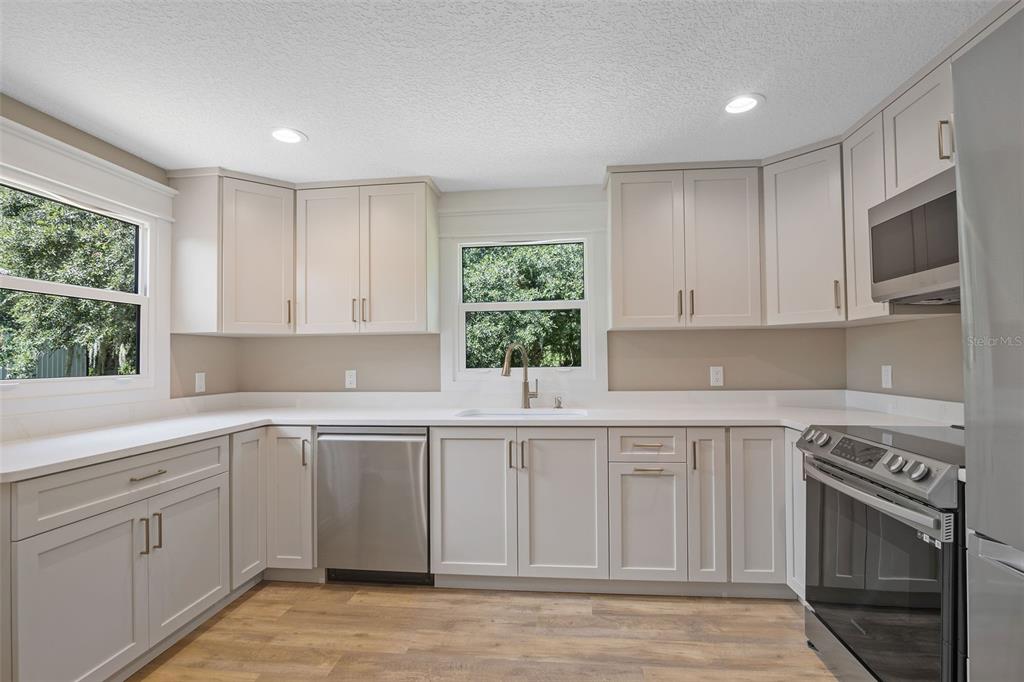 A kitchen features light gray cabinets, stainless steel appliances, white countertops, and wood-look flooring — 2463 PIONEER TRAIL, NEW SMYRNA BEACH, FL