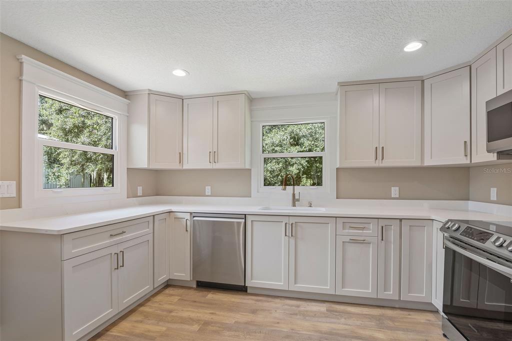 A kitchen features light gray cabinets, white countertops, stainless steel appliances, and wood-look flooring — 2463 PIONEER TRAIL, NEW SMYRNA BEACH, FL