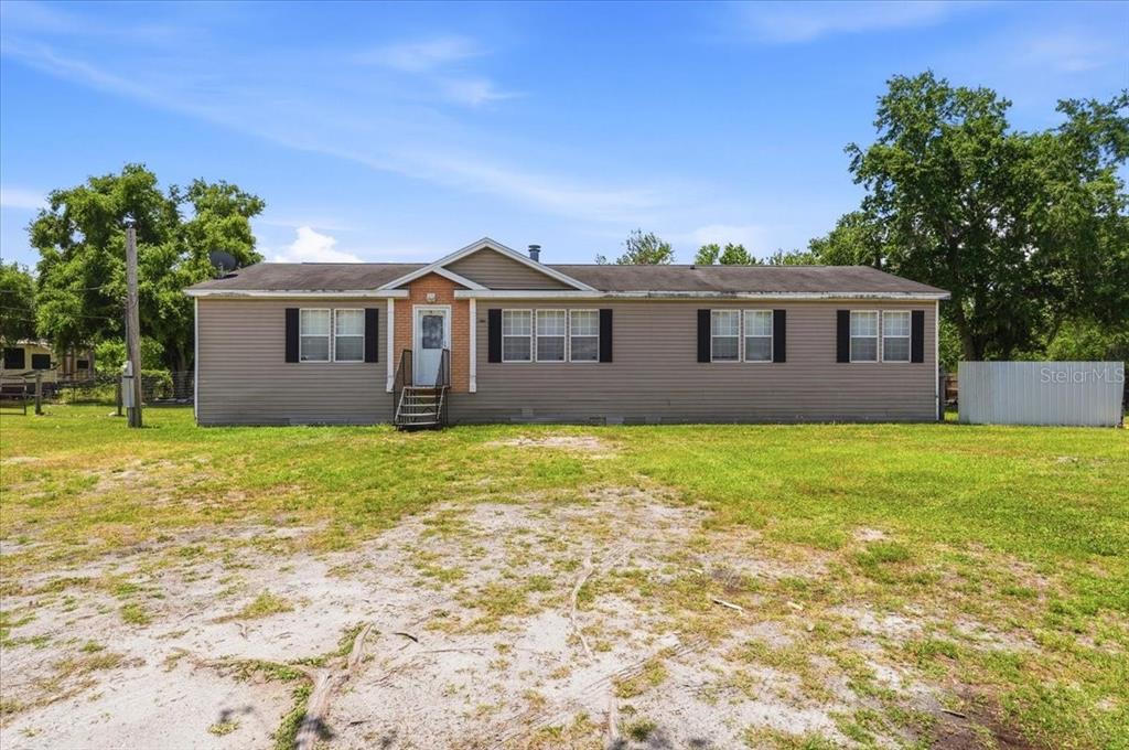 A single-story manufactured home with beige siding sits on a large, grassy lot — 10724 PATHFINDER TRAIL, LAKELAND, FL