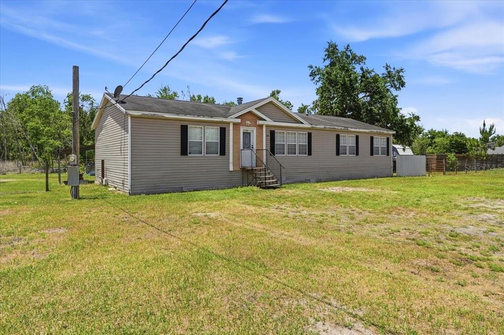 A single-story house with beige siding sits on a large, grassy lot with trees — 10724 PATHFINDER TRAIL, LAKELAND, FL