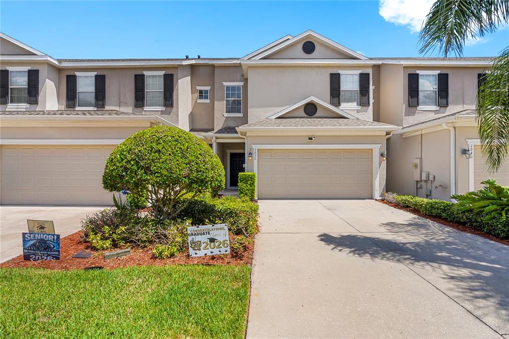 A two-story townhouse with a beige stucco exterior, a two-car garage, and graduation signs — 1936 COMPASS FLOWER WAY, OCOEE, FL