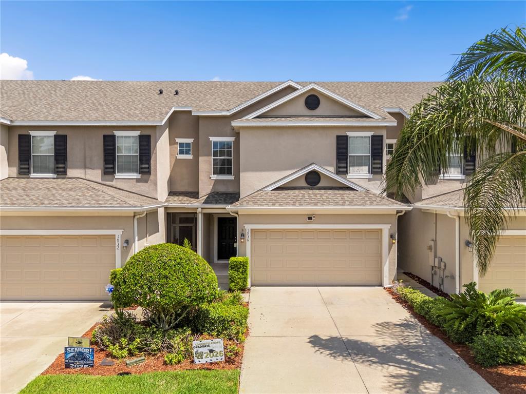 A two-story townhouse exterior with beige stucco, a two-car garage, and a small front garden — 1936 COMPASS FLOWER WAY, OCOEE, FL