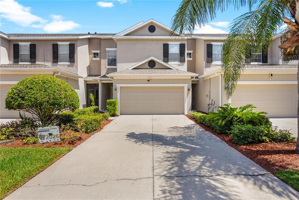 A two-story townhouse exterior features a beige facade, a two-car garage, and a concrete driveway — 1936 COMPASS FLOWER WAY, OCOEE, FL