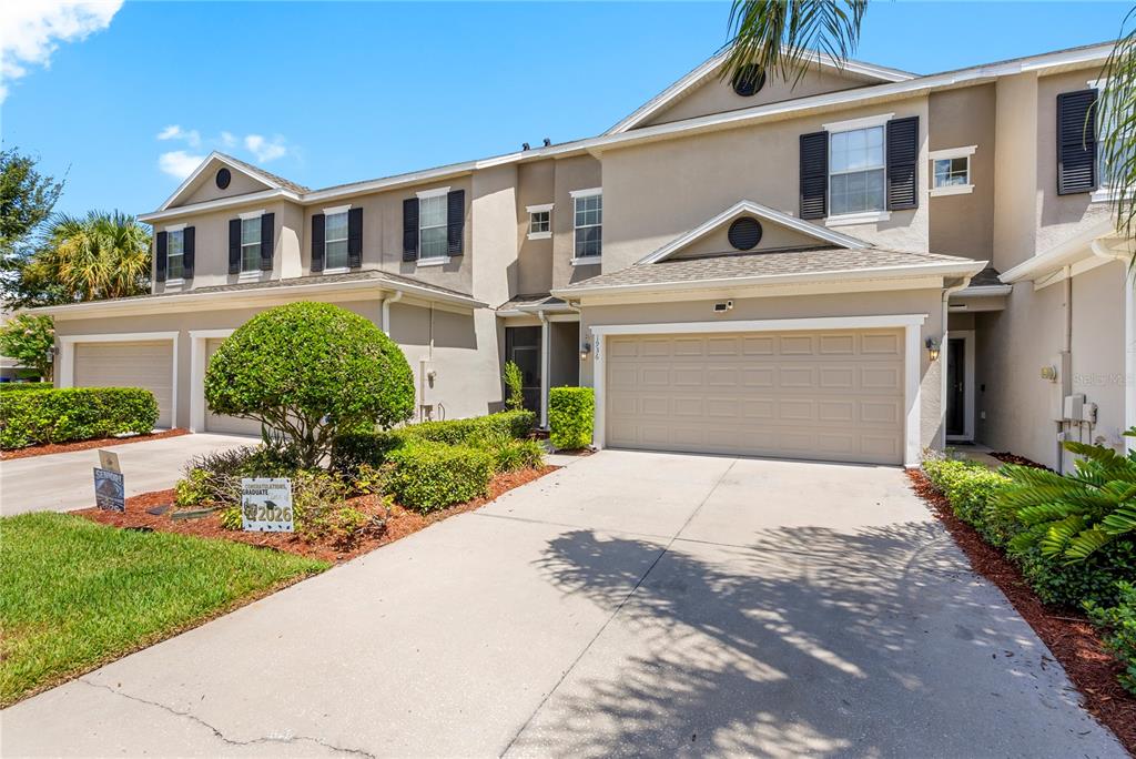 A two-story townhouse with a beige stucco exterior, a two-car garage, and a landscaped front yard — 1936 COMPASS FLOWER WAY, OCOEE, FL