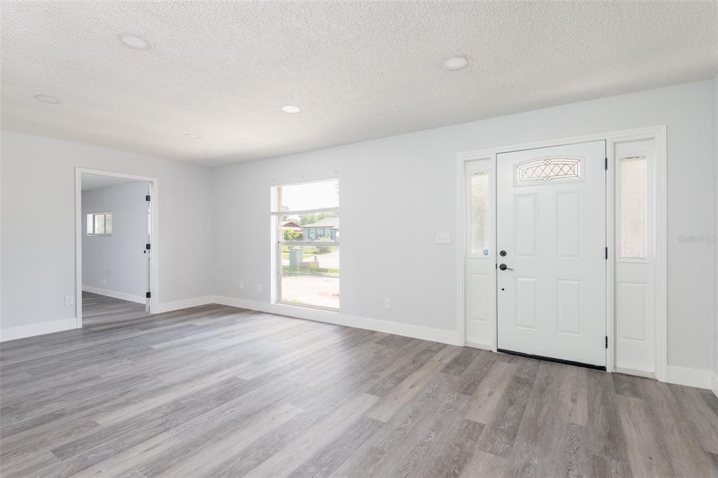 A bright living room features light gray walls, wood-look flooring, a front door, and a window — 902 SHANGRI LA DRIVE, SEFFNER, FL