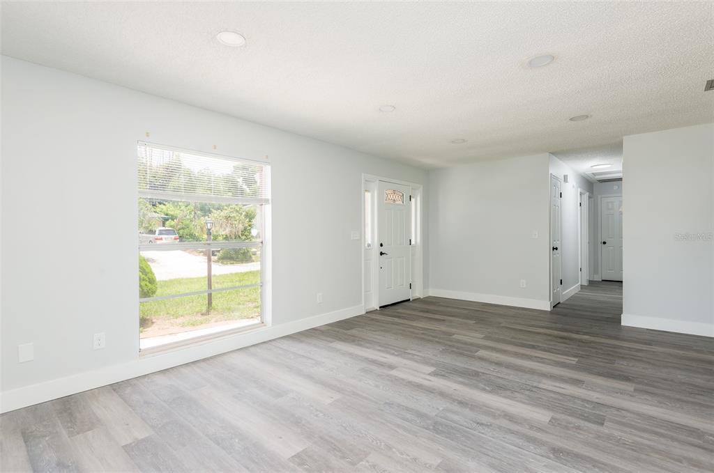 A bright, empty living room features light gray walls, wood-look flooring, and a front door — 902 SHANGRI LA DRIVE, SEFFNER, FL