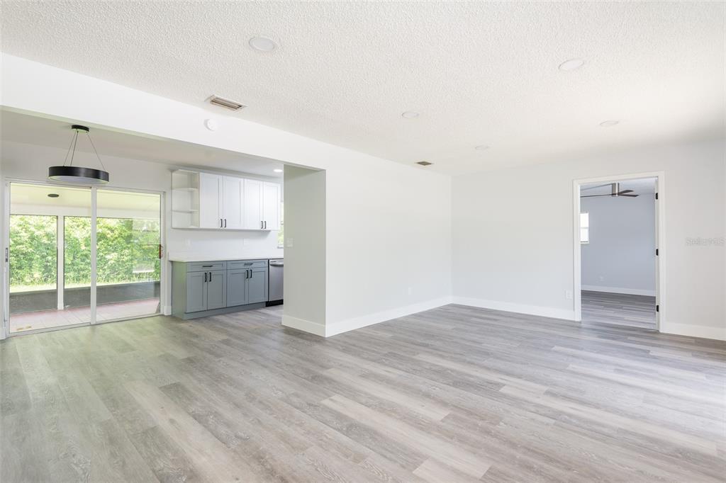 A living area with gray wood-look flooring, recessed lighting, and an adjacent kitchen with cabinets — 902 SHANGRI LA DRIVE, SEFFNER, FL