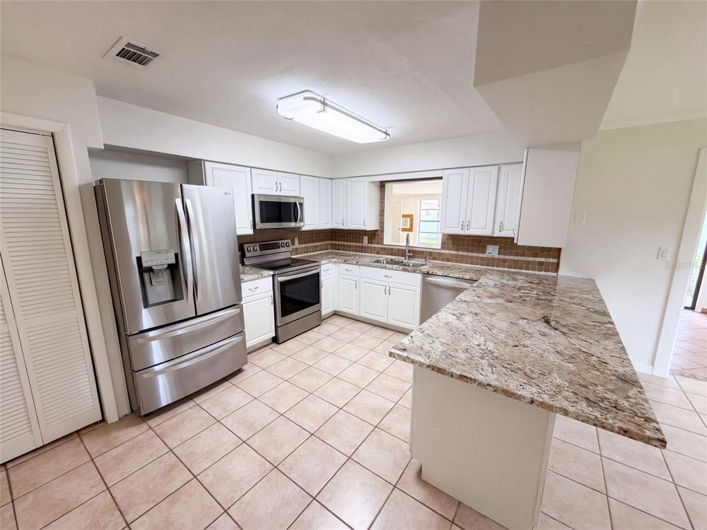A kitchen features white cabinets, granite countertops, stainless steel appliances, and light-colored tile flooring — 2617 S FAIRWAY DRIVE, MELBOURNE, FL