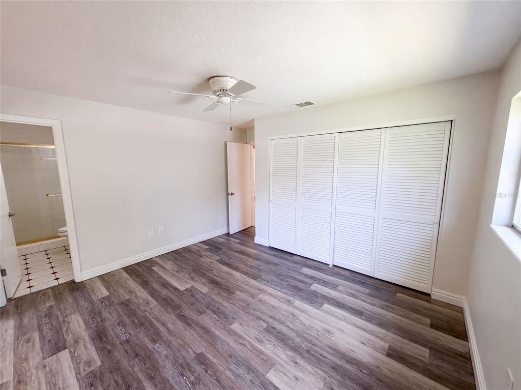 A bedroom with light walls, wood-look flooring, a ceiling fan, and white louvered closet doors — 2617 S FAIRWAY DRIVE, MELBOURNE, FL