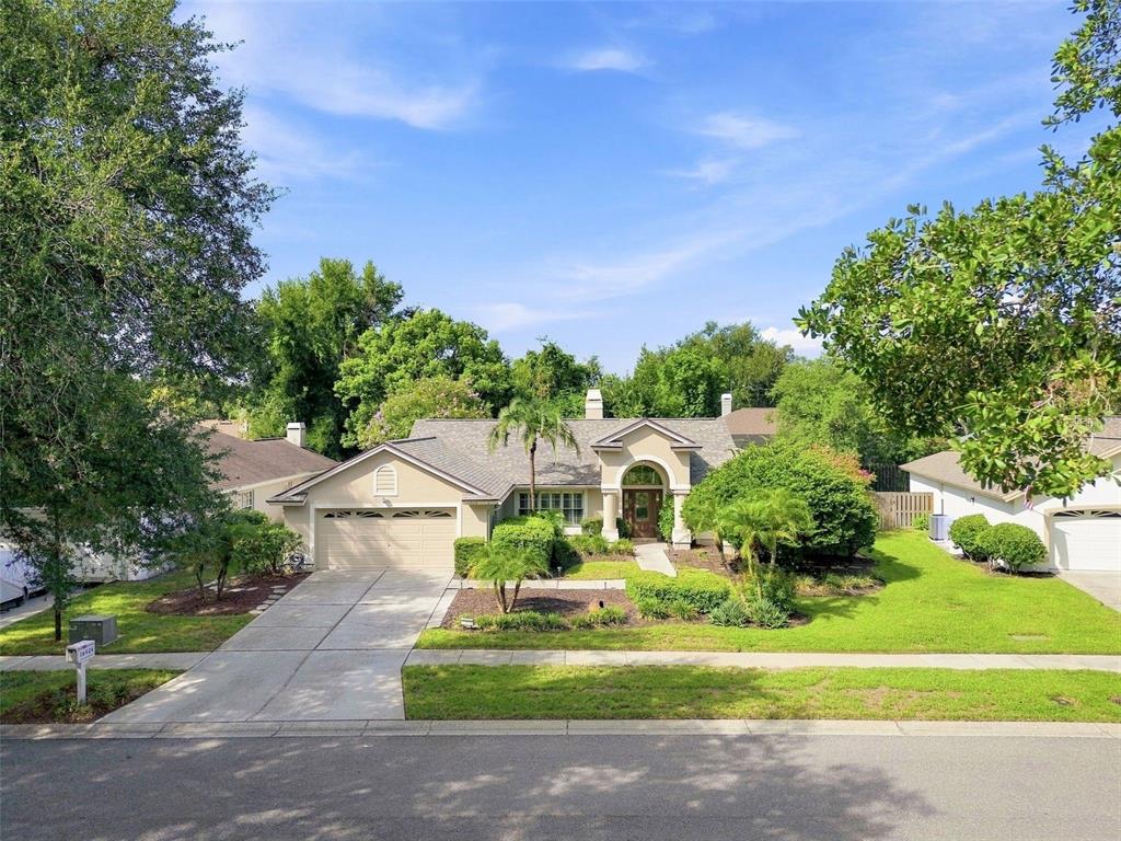 A single-story house with a beige exterior, a two-car garage, and a landscaped front yard — 16804 SHEFFIELD PARK DRIVE, LUTZ, FL