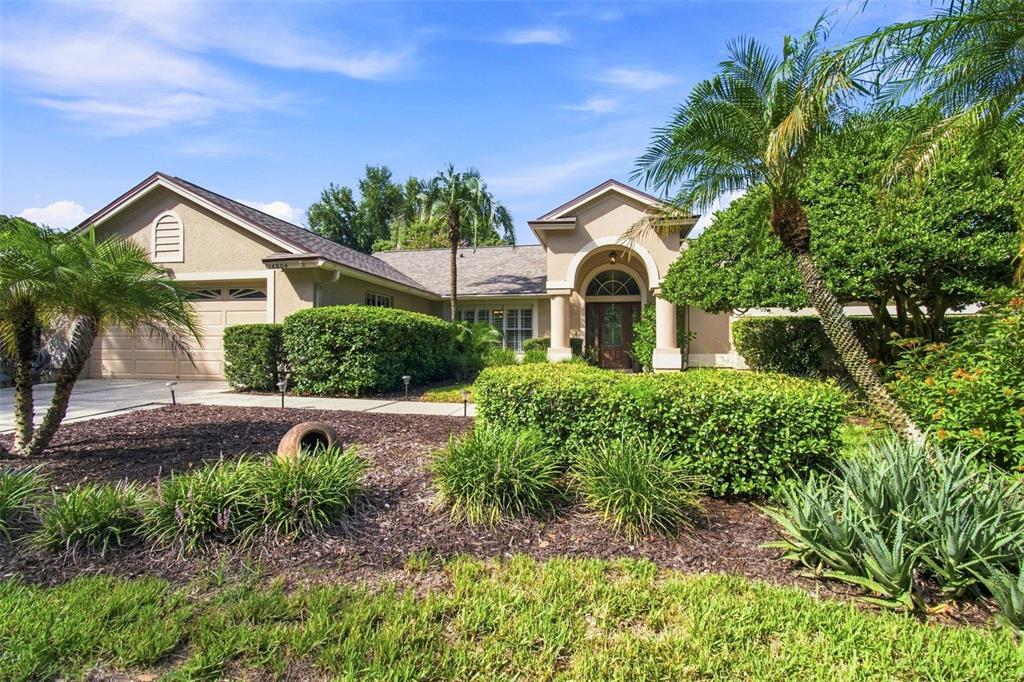 A single-story house with a beige exterior, a two-car garage, and a landscaped front yard — 16804 SHEFFIELD PARK DRIVE, LUTZ, FL
