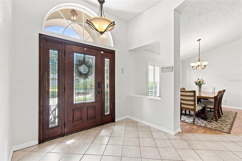A wooden front door with glass panels and sidelights sits beside a large green shrub — 16804 SHEFFIELD PARK DRIVE, LUTZ, FL