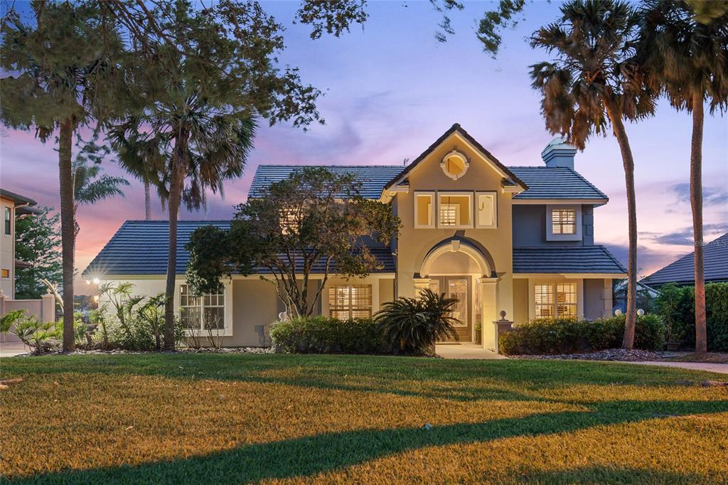 A two-story house with a tiled roof, arched entryway, and palm trees at dusk — 9620 MAYWOOD DRIVE, WINDERMERE, FL