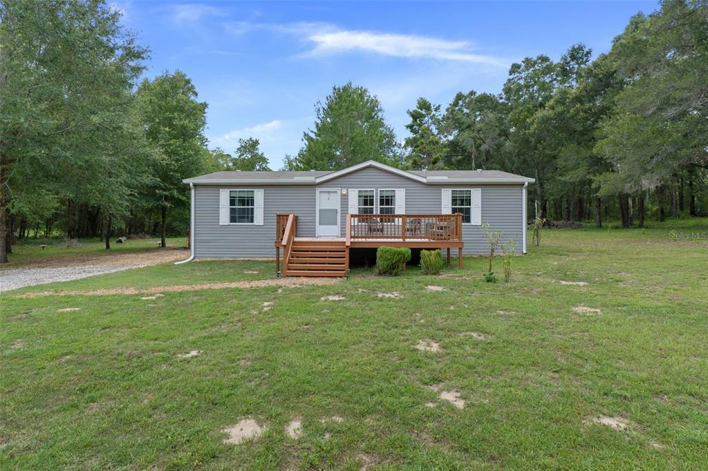 A gray manufactured home with a wooden deck sits on a grassy lot with trees — 840 N OBRIEN POINT, LECANTO, FL