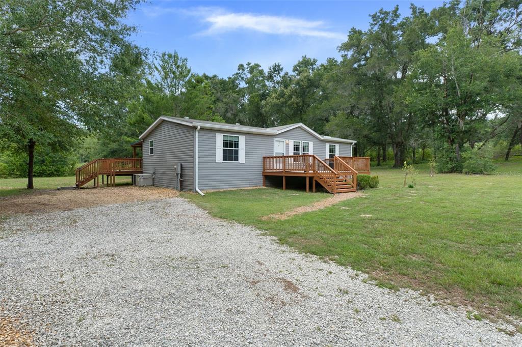 A gray manufactured home with wooden decks sits on a gravel driveway surrounded by trees — 840 N OBRIEN POINT, LECANTO, FL