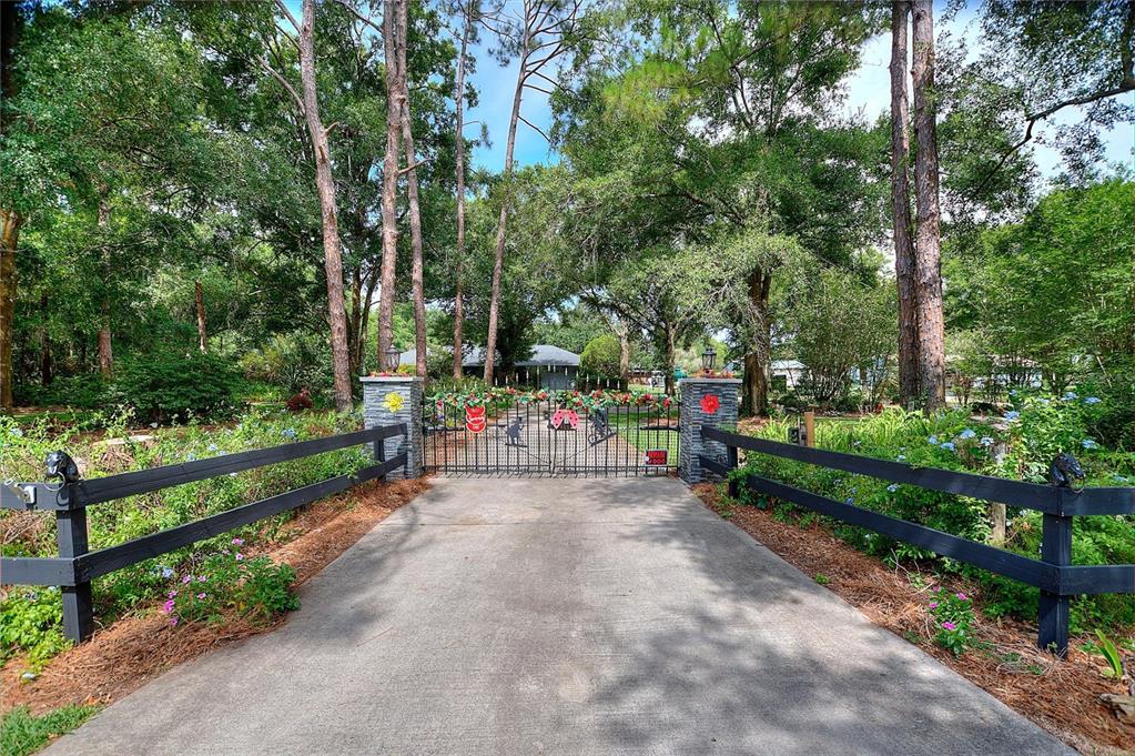 A paved driveway leads to a gated entrance flanked by stone pillars and wooden fencing — 7 LAKE ARROWHEAD DRIVE, WINTER HAVEN, FL