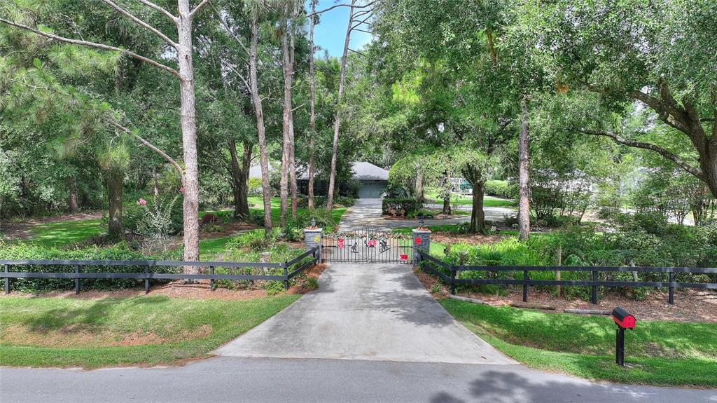A gated concrete driveway leads to a house surrounded by many tall trees and greenery — 7 LAKE ARROWHEAD DRIVE, WINTER HAVEN, FL