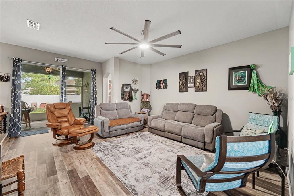 A living room features a ceiling fan, gray sofas, a leather recliner, and a sliding door — 13144 LAUREL CREST COURT, GRAND ISLAND, FL